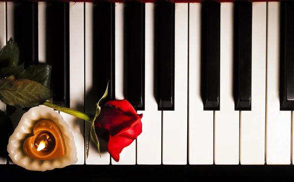 Rosa roja y vela en las teclas de piano — Foto de Stock