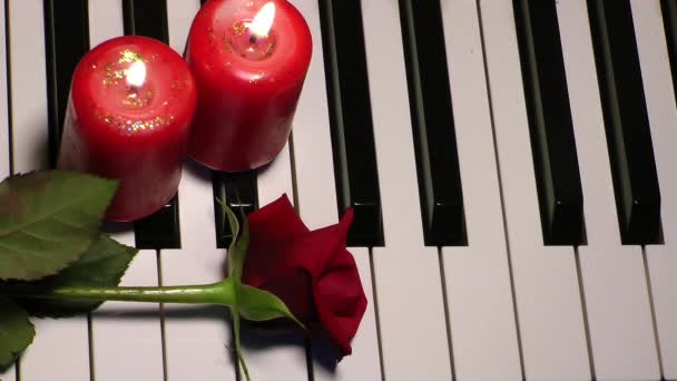 Роза і свічка на клавішах фортепіано — стокове відео