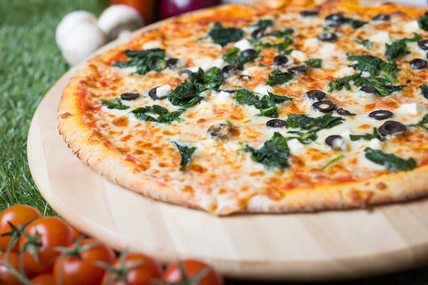 Baked Italian pizza with cheese, vegetables, meat and herbs on the grass — Stock Photo, Image