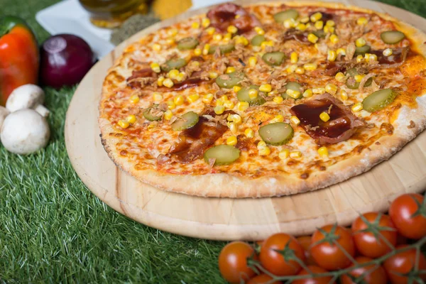 Baked Italian pizza with cheese, vegetables, meat and herbs on the grass — Stock Photo, Image