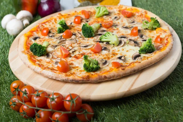 Baked Italian pizza with cheese, vegetables, meat and herbs on the grass — Stock Photo, Image