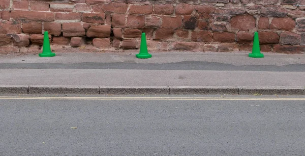 Three green plastic traffic cones beside road against historic wall — Stock Photo, Image