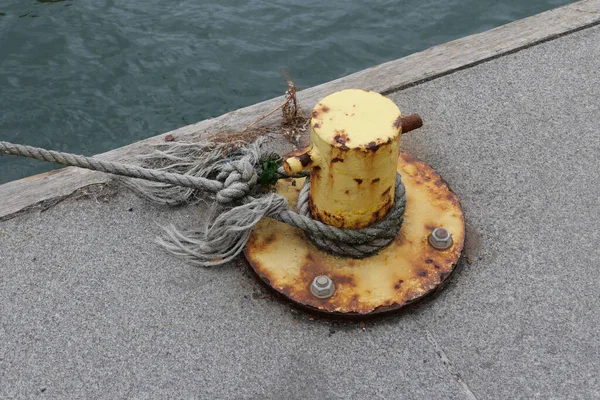 Yellow rusting painted bollard with fraying rope attached beside water