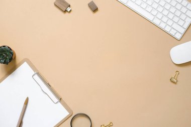 Temiz bir kağıda sahip bir tablet bej bir arka planda, bilgisayar ve malzemelerle dolu bir masadır. Üst görünüm ve kopyalama alanı