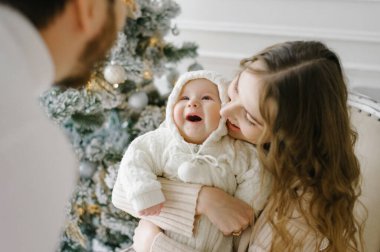 Bir anne, babasına gülümseyen küçük bir çocuğu kollarında tutar. Bebeğe odaklanmaya çalış. Mutlu aile Noel 'i Noel ağacında kutluyor.