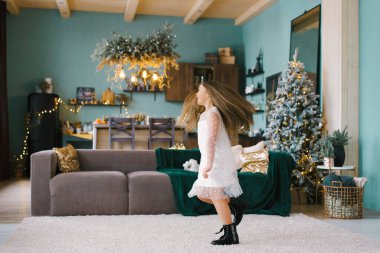 Beyaz tül elbiseli ve siyah ayakkabılı güzel bir kız, Noel ve yeni yıl için dekore edilmiş, naneli duvarları olan şık bir oturma odasında dönüyor.