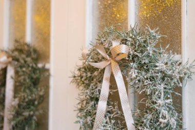 Bir kır evinin beyaz kapısında saten bir fiyonk ve şık bir Noel çelengi.