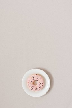 Minimalist tatlılık bayrağı. Bej arka planda beyaz bir tabakta pembe çörek ve fotokopi alanı. Sabah mı akşam mı tatlı mı? Günlük için arkaplan