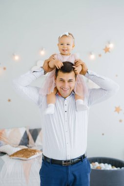 Mutlu baba, bir yaşındaki kızını çocuk odasında boynuna asıyor. Mutlular.