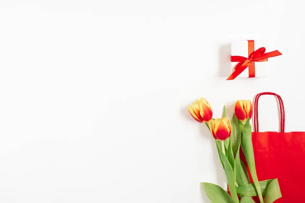 コピースペースの白い背景に贈り物と赤い紙の袋の近くに赤い黄色のチューリップとフラットレイ組成物 バレンタインデー誕生日母の日 — ストック写真