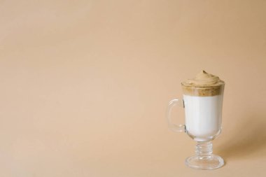 Güzel bir dalgon, bej arka planda şeffaf bir kupada köpüklü kahve içer.