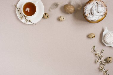 Paskalya pastası, yumurta, bir fincan çay, tatlılar, çiçek açan elma ağacının dalları ve bej arkaplanda tüyler. Uzayı kopyala, düz yat
