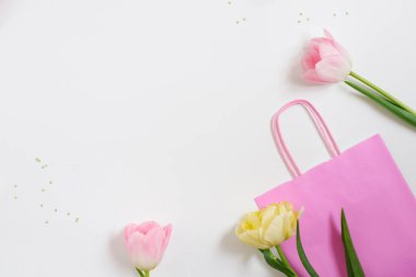 Güzel bahar pembe ve sarı laleler beyaz renkli parlak çantalı beyaz kurdeleli çiçekler. Düz yatıyordu. Uzayı kopyala Kadınlar Günü ya da Sevgililer Günü hediyesi. Mağazada veya online alışverişte tatil bahar indirimi kavramı