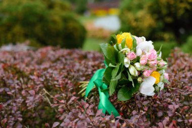 Düğün buketi pembe güller ve sarı çalıların üzerinde yatıyor.
