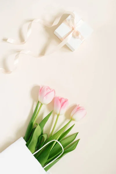 ペーパーバッグにピンクチューリップとベージュの背景に弓で贈り物とフラットレイ組成物 バレンタインデー 母の日 誕生日のグリーティングカード 春のコンセプト — ストック写真