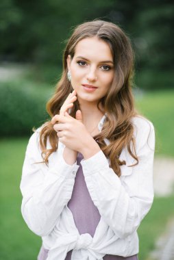 Çıplak makyajlı, doğal yeşil bir arka planda uzun dalgalı saçlı güzel bir genç kadın.