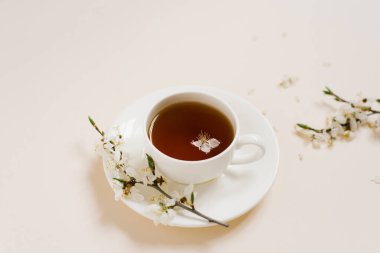 Siyah çay ve marşmelovlu beyaz porselen bardak. Çiçek açan bir elma ağacının dalları bej bir arka planda yatar. Bahar konsepti