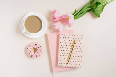 Kadın blogcular için modaya uygun bir konsept: pembe günlük, defter, donat, pembe laleler ve bej arka planda bir fincan kahve. Evden çalışmak
