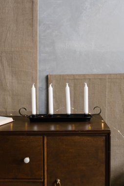 Siyah bir şamdanın üzerindeki beyaz ince mumlar kahverengi tahta bir çekmecenin üzerinde duruyor. Neo-klasik dekor ya da klasik iç mekan elementleri