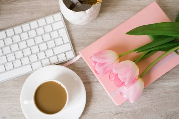 Pink tulips with a festive spring mood and coffee on a wooden table Women\'s work, home office and career concept. Top view. Copy space