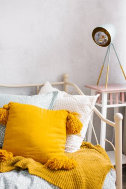 Turuncu yastığın yakın çekimi, yatak odasındaki yatak başlığı ve yatak odasının iç tarafındaki yatağın yanındaki gece lambası.