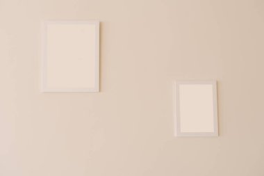Farklı boyutlarda bej bir duvarda beyaz model çerçeveler.
