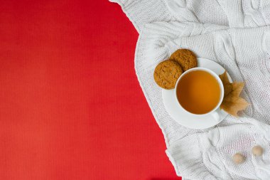 Sonbahar kompozisyonu, bir fincan çay ve sarı sonbahar yapraklı Uçan Kadın. Çay molası zamanı. Kırmızı arka planda parlak yapraklı örülü battaniye ve kurabiyeler. Boşluğu Kopyala