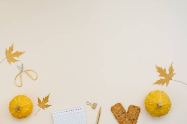 Sarı balkabağı, düşmüş yapraklar, kurabiyeler, makas, defter ve kalemle sonbahar arkaplanı. Blogcu, öğrenci, okul çocuğu veya serbest çalışan için çalışma yeri