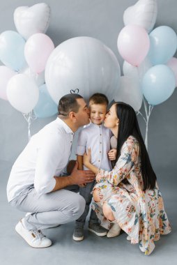 Cinsiyet belirleme partisi. Doğmamış çocuğun cinsiyetini belirlemek için popo topunun arka planında ikinci çocuklarını bekleyen genç bir aile. Ebeveynler en büyük oğullarını yanağından öperler.