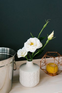 Beyaz bir seramik vazo ve içinde yapay beyaz bir Eustoma çiçeği. Yemek odasında ya da mutfakta dekor var.