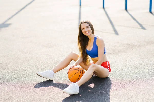 Atrakcyjna Sportowa Młoda Kobieta Zewnątrz Pozowanie Siedzi Boisko Koszykówki Gospodarstwa — Zdjęcie stockowe