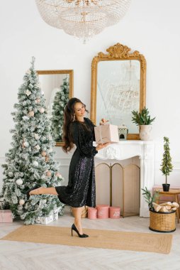 Mutlu bir kadın elinde bir Noel hediyesi tutar ve Noel ağacında açar.