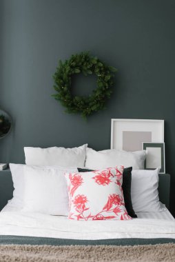 Yatakta yastıklar ve üzerinde siyah bir duvarda asılı bir Noel çelengi.