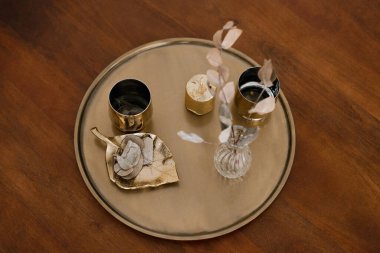 Altın bardaklar, kahve masasındaki yuvarlak tepside vazoda kurumuş çiçekler. Üst görünüm