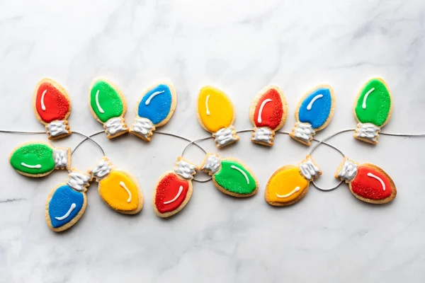 Christmas lightbulb cookies on a string against a marble background. — Stock Photo, Image