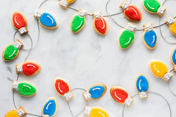 Christmas lightbulb cookies on string forming a border frame with copy space in the middle, against a light background. — Stock Photo, Image