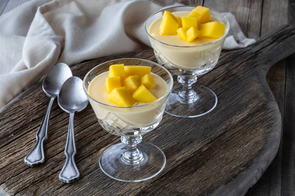 Mango mousse dessert parfaits in crystal goblets on a wooden board ready for eating.