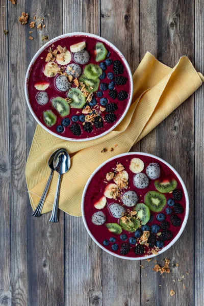Top down view of acai berry bowls garnished with various sliced fruit and topped with granola. — Stock Photo, Image