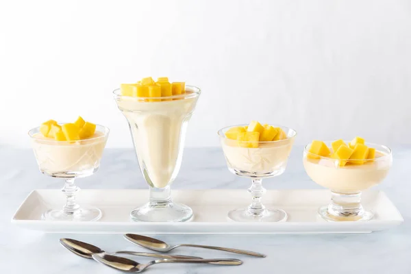A row of mango mousse parfaits in different glass dessert dishes ready for serving.