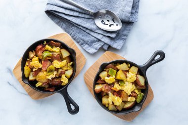 Mermer bir masada kahvaltı tavasıyla doldurulmuş iki dökme demir kızartma tavasının yukarıdan görünüşü.