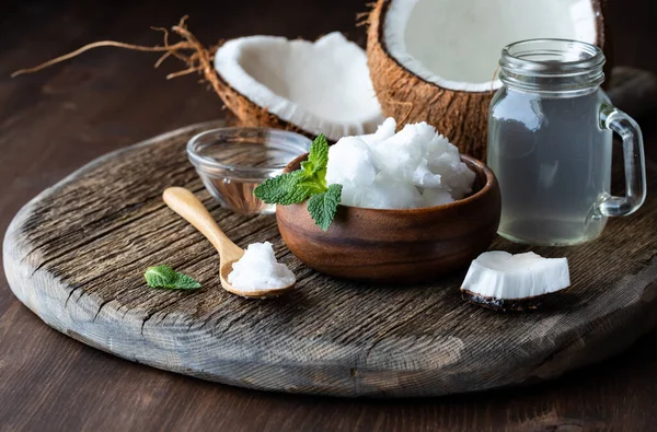 Vista de perto do óleo de coco, triglicéridos de cadeia média MTC e água de coco com um coco rachado ao meio atrás. — Fotografia de Stock