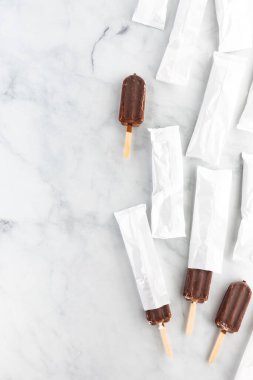 Sıralar dolusu çikolatalı vanilyalı dondurma paketler halinde, paketten birkaç tane çıkıyor ve ikisi de tamamen dışarı çıkıyor..