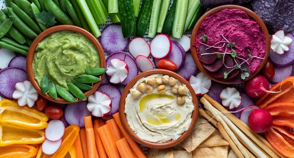 Tepeden tırnağa üç renkli humus sosu çeşitli kesilmiş sebzeler, pide ısırıkları ve ekmek çubuklarıyla çevrili..