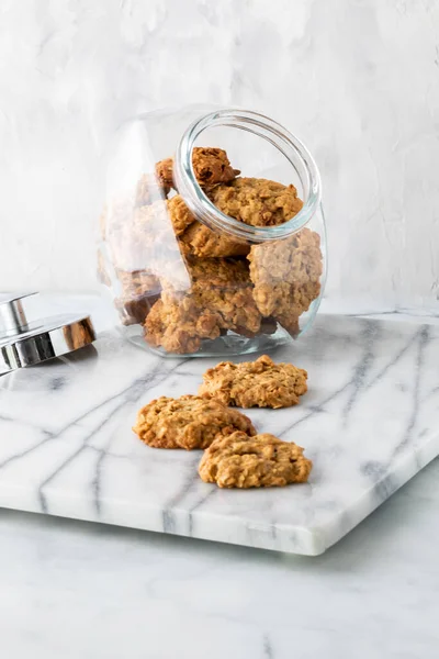 Glass cookie jar filled with oatmeal raisin cookies with three cookies in front.