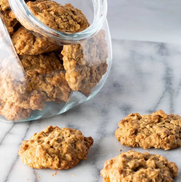 Glass cookie jar filled with oatmeal raisin cookies on a marble slab.