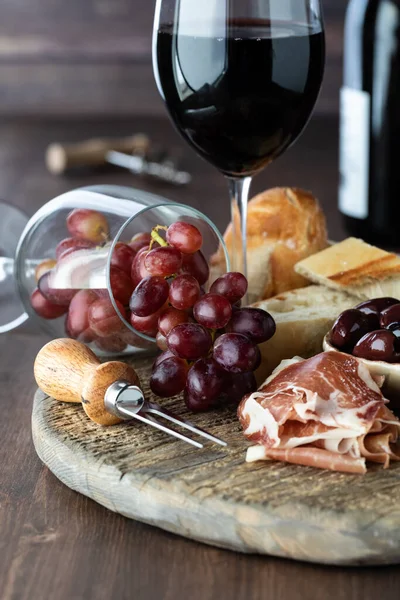 Placa de charcutaria rústica com vinho tinto e uvas contra um fundo de madeira. — Fotografia de Stock