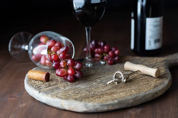 Przewrócony kieliszek do wina z czerwonymi winogronami wylewający się na rustykalną deskę z kolejną szklanką wypełnioną czerwonym winem. — Zdjęcie stockowe