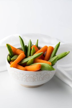 Taze bezelye ve havuçları küçük beyaz bir kasede atıştırmaya hazır hale getir..