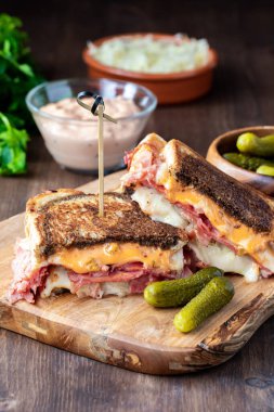 Tahtada Rus sosu, lahana turşusu ve dereotu turşusuyla birlikte kızarmış Reuben sandviçi..