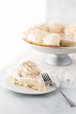 Arkasında turta olan bir dilim muzlu kremalı turtayı parlak güneşli bir pencereye yaklaştır..